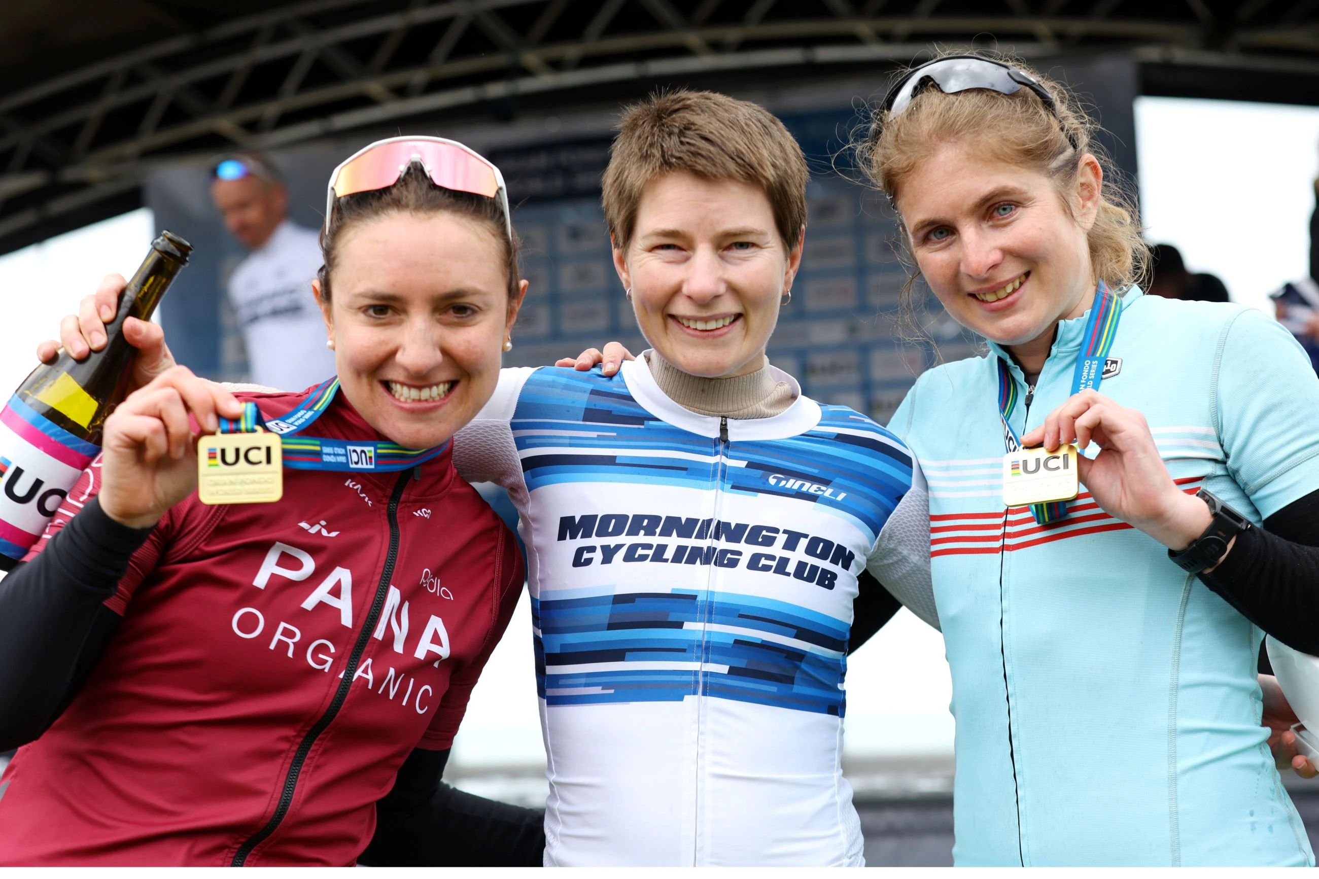 Three female cyclists pose in front of the podium of the 2024 Amy's Gran Fondo, two of them with UCI medals indicating they have qualified for the UCI Gran Fondo World Championships. (Con Chronis)
