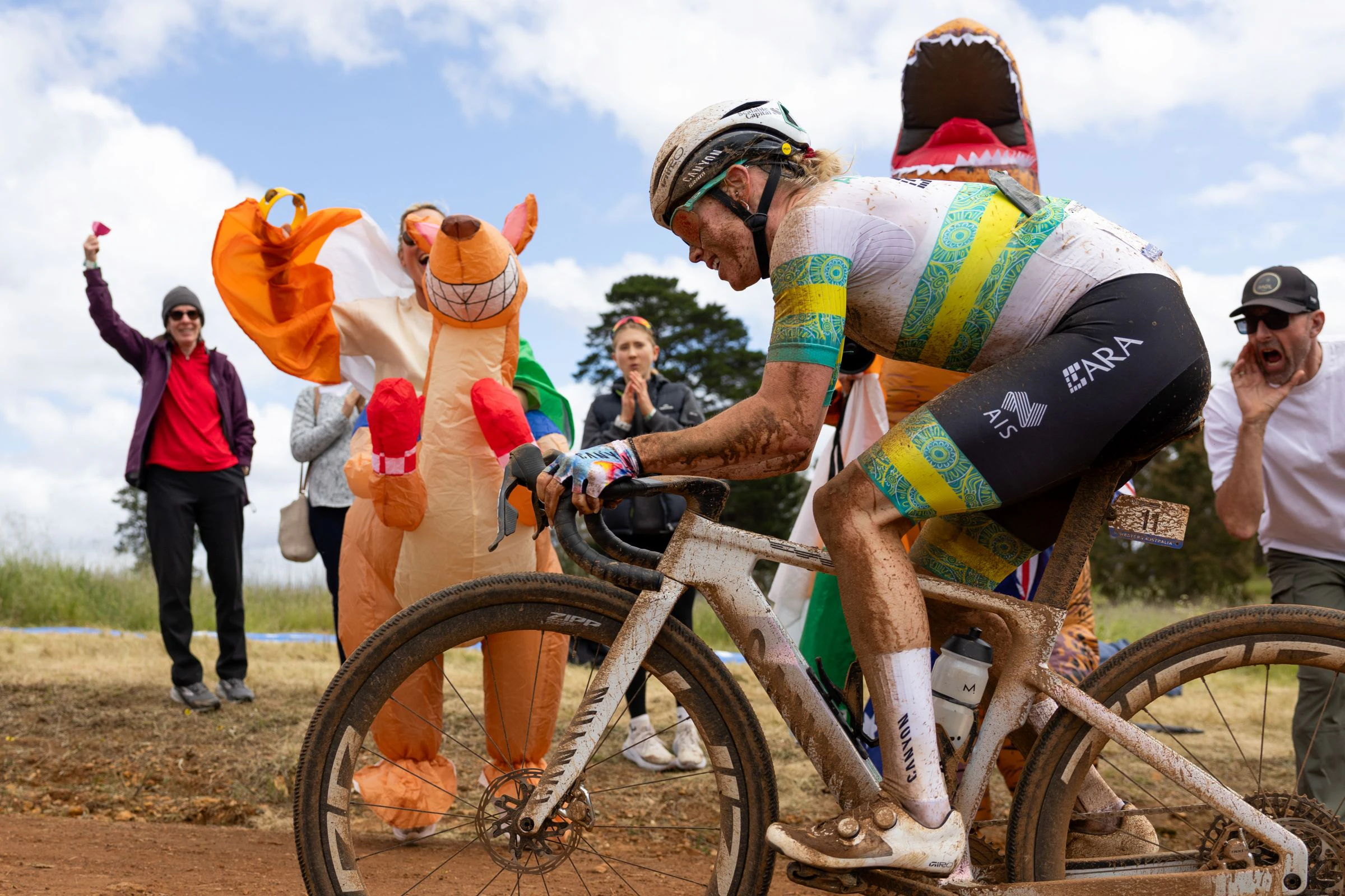 Tiffany Cromwell, ARA Australian Cycling Team athlete, races past a fan in a dinosaur costume and a kangaroo costume at the 2026 UCI Gravel World Championships in Nannup, Western Australia
