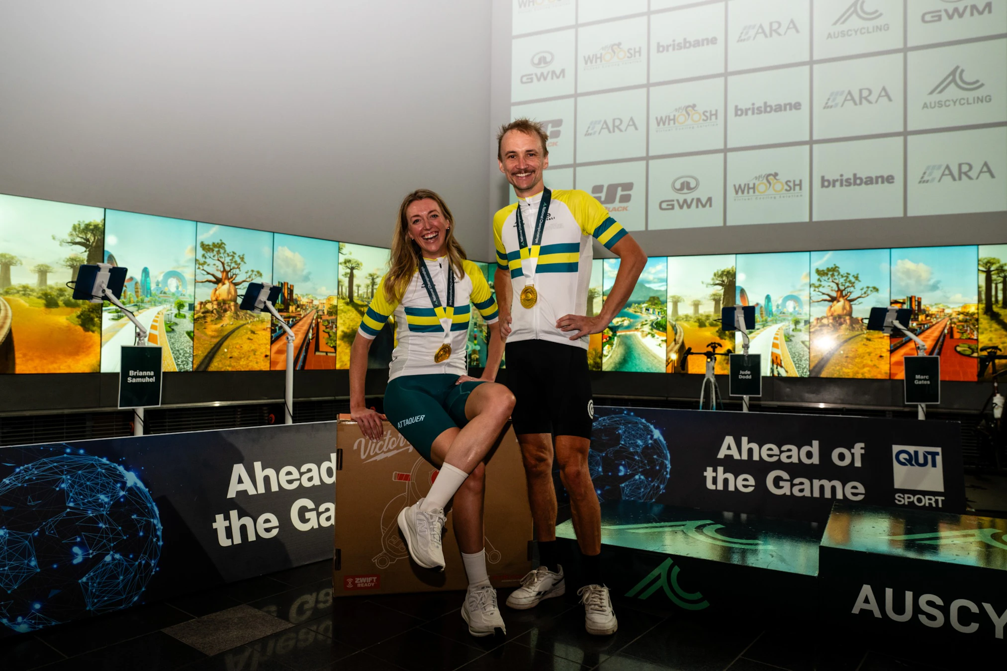Matilda Field and Josh Harris pose with their green-and-gold jersey as cycling esports national champions of 2026 at QUT's The Cube in Brisbane at the 2026 AusCycling Esports National Championships
