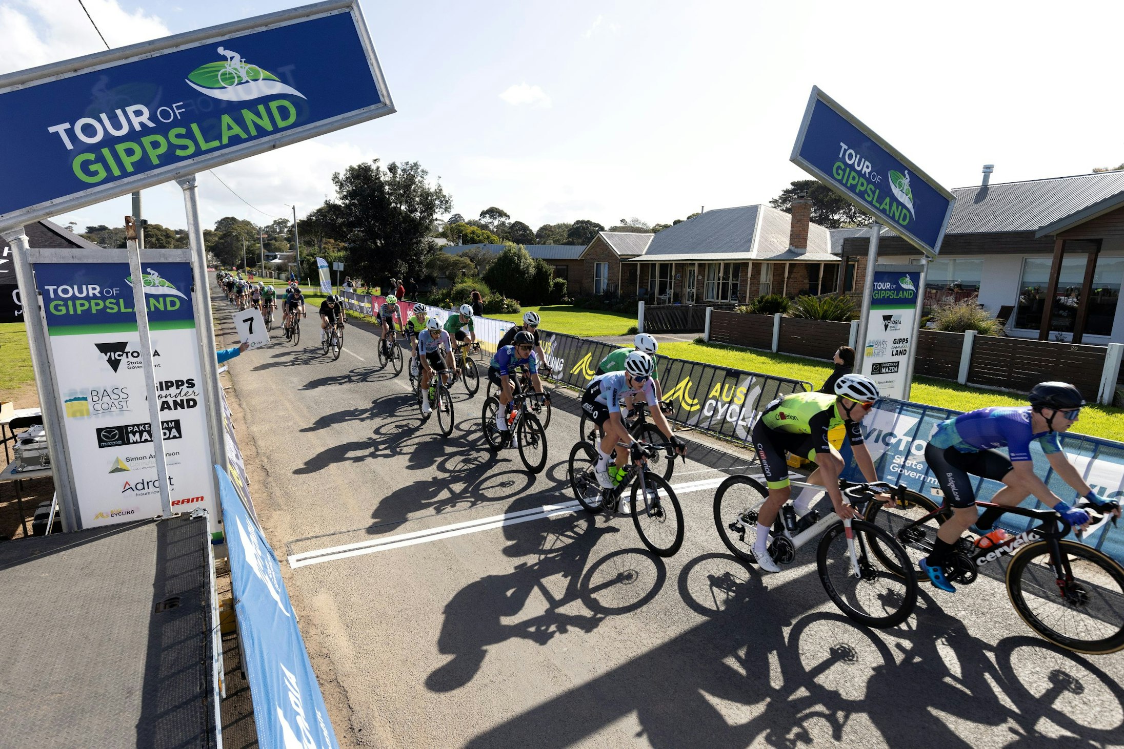 The men's National Road Series peloton (NRS) ride through the start-finish line at the 2023 Tour of Gippsland criterium in Rhyll, Phillip Island, Victoria. Photo by Con Chronis.