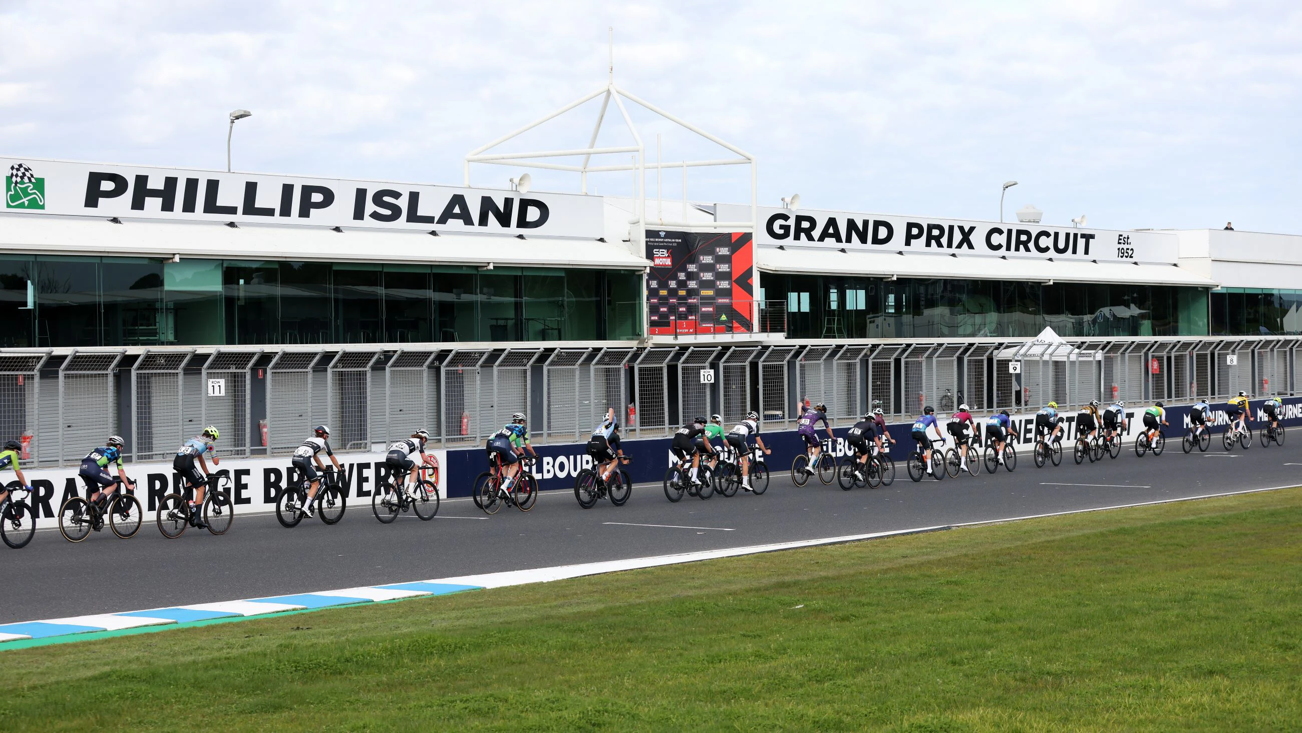 The men's National Road Series peloton strung out on the Phillip Island Grand Prix Circuit as it passes the pit building and podium used for motor racing in Victoria, Australia