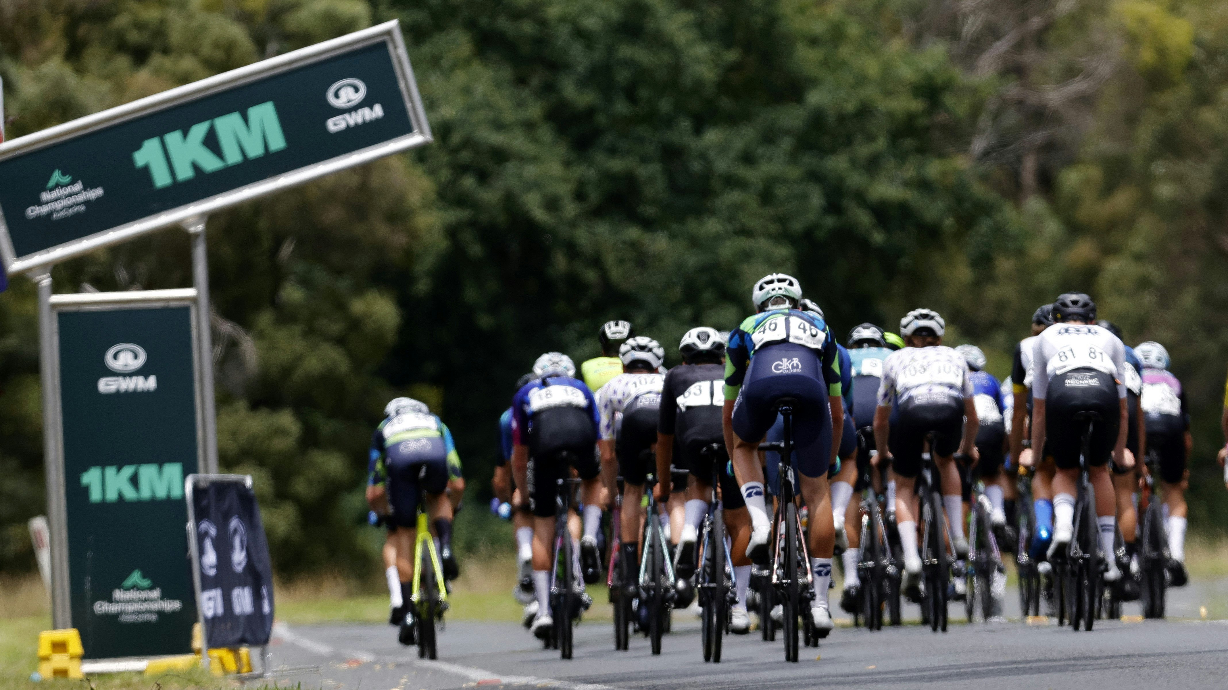 Australian road cyclists passing the one kilometre (1km) remaining banner in the AusCycling Road National Championships