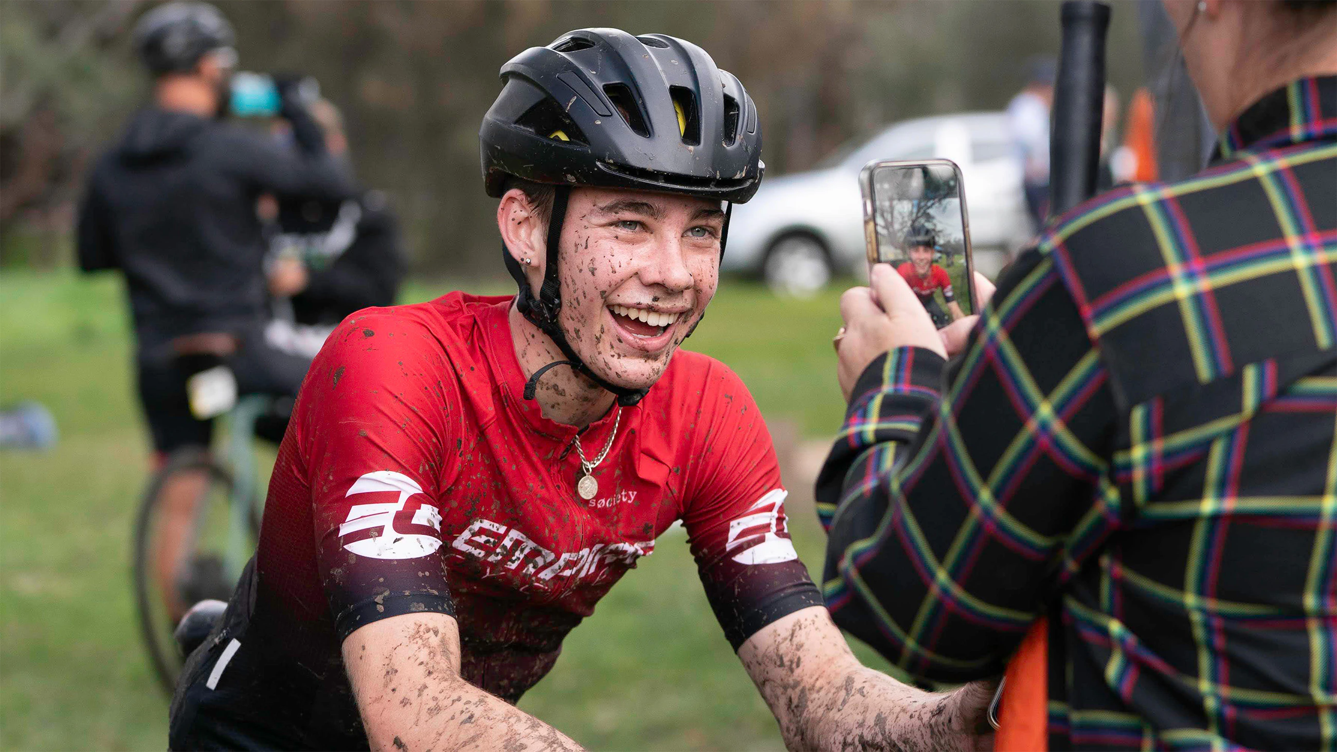 West Australian junior cyclist Cooper Dunlop smiles as he poses for a photo being taken by his mother after a muddy cyclo-cross race (photo by Toby Brown AusCycling)