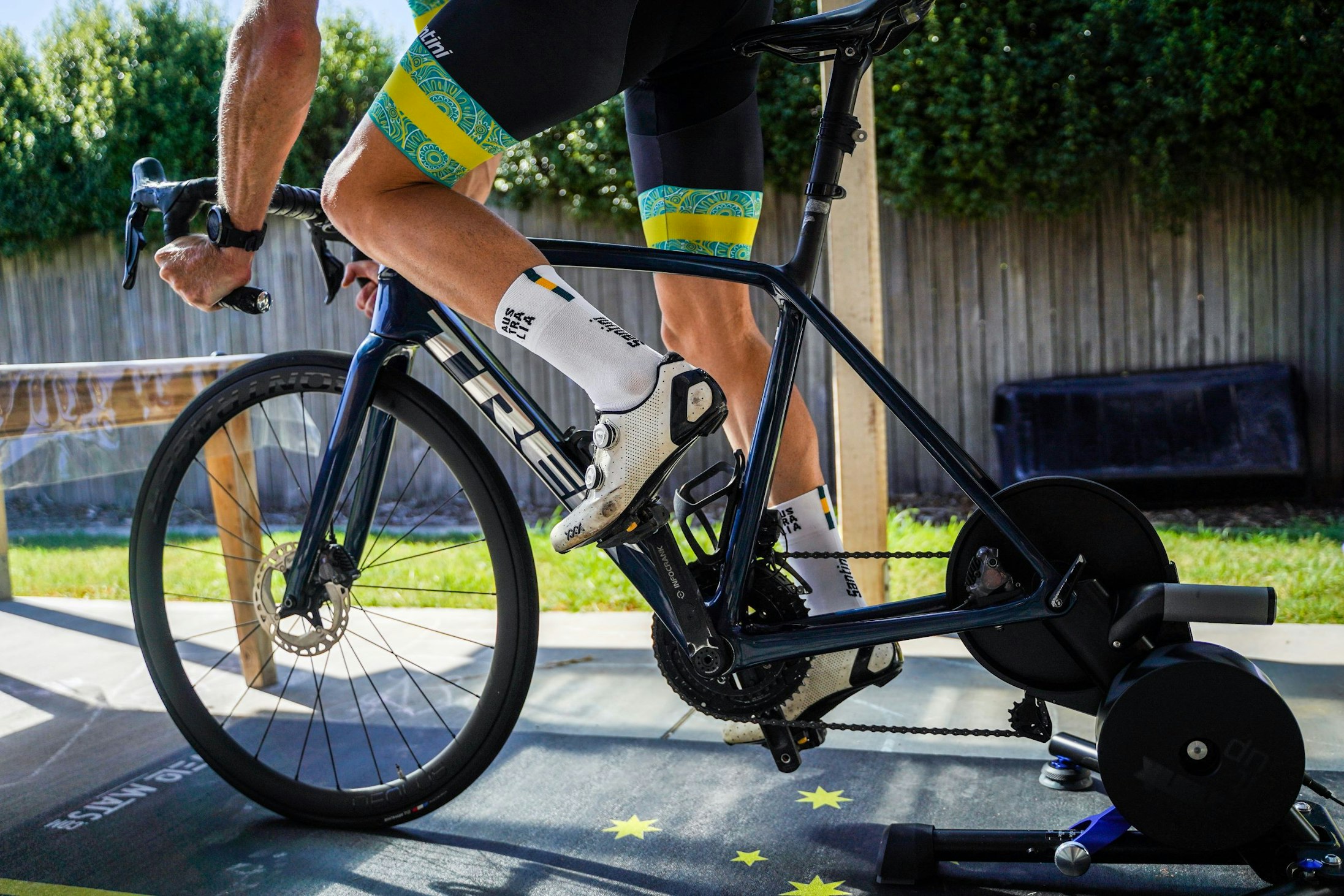 An unidentified Australian Cycling Team cyclist riding on a stationary trainer on a backyard porch