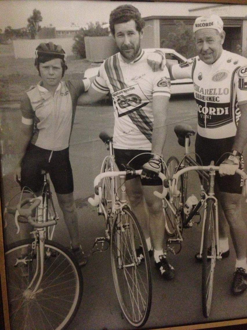 A black-and-white photo of Perth road cyclist Ryan Suckling as a child, standing astride a bicycle alongside his father Gary Suckling and grandfather Owen Suckling, likely taken during the 1980s.