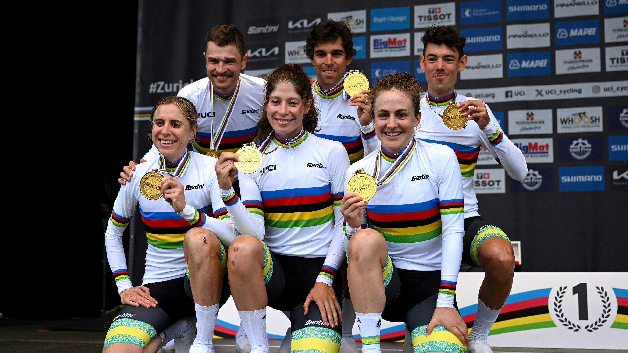 Jay Vine, Michael Matthews, Ben O'Connor, Brodie Chapman, Ruby Roseman-Gannon and Grace Brown pose in rainbow jerseys with gold medals on the podium of the 2024 UCI Road Mixed Relay Team Time Trial World Championships in Zurich, Switzerland.