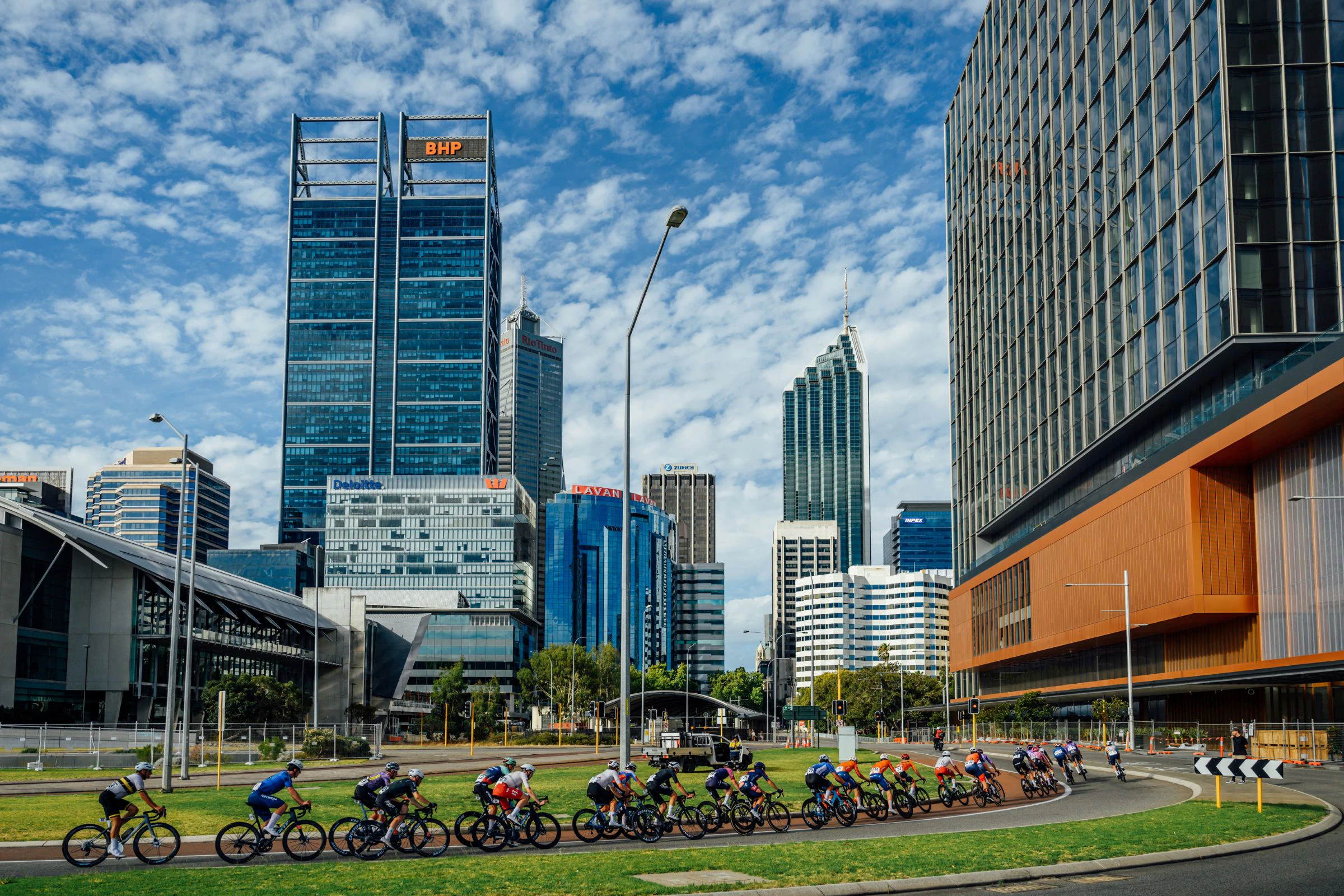 The men's road race peloton passes near Elizabeth Quay with the buildings of Perth CBD looming over them during the Westbridge Funds Road National Championships in Perth, 2026
