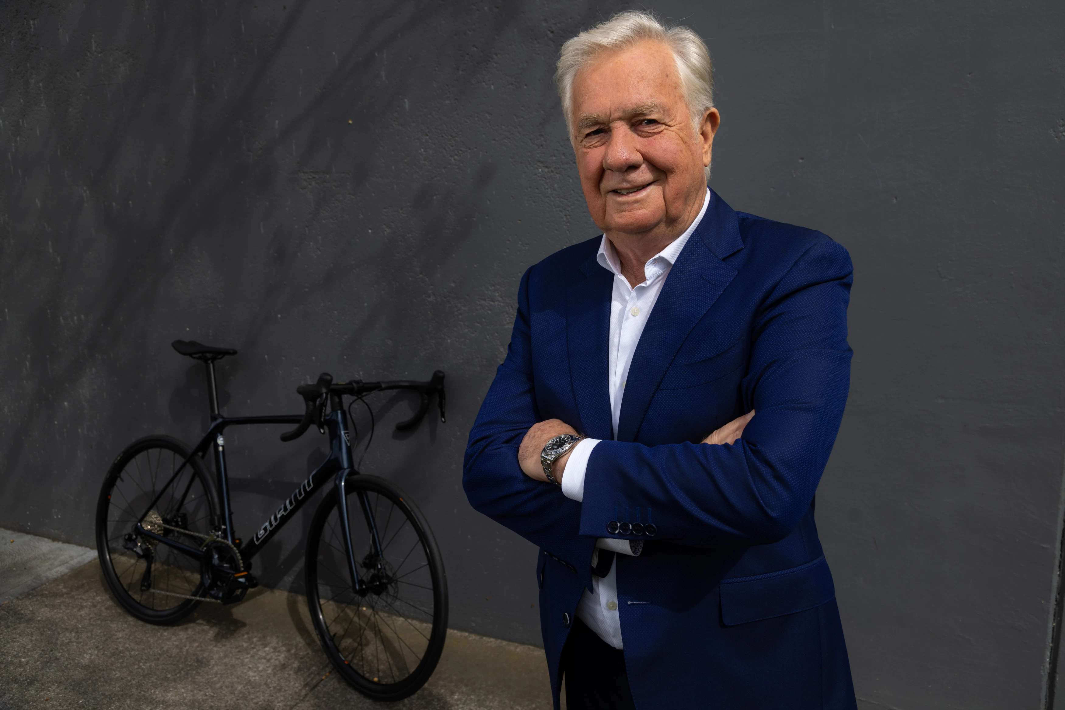Australian businessman and cycling philanthropist Gerry Ryan posing in a suit jacket while standing next to a bicycle