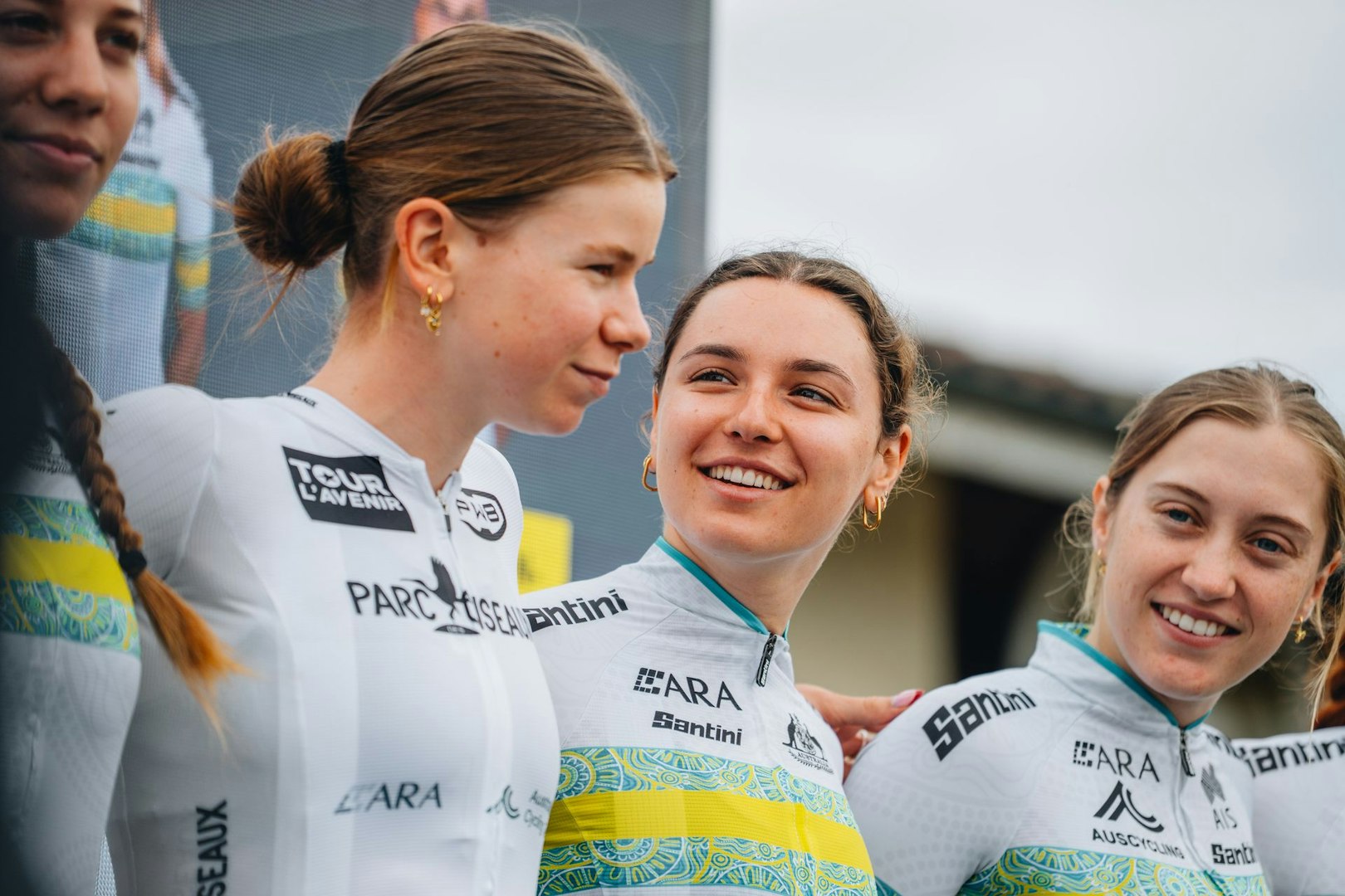 Sophie Marr smiles as Talia Appleton looks focused at a team presentation with the ARA Australian Cycling Team during the 2025 Tour de l'Avenir Femmes.