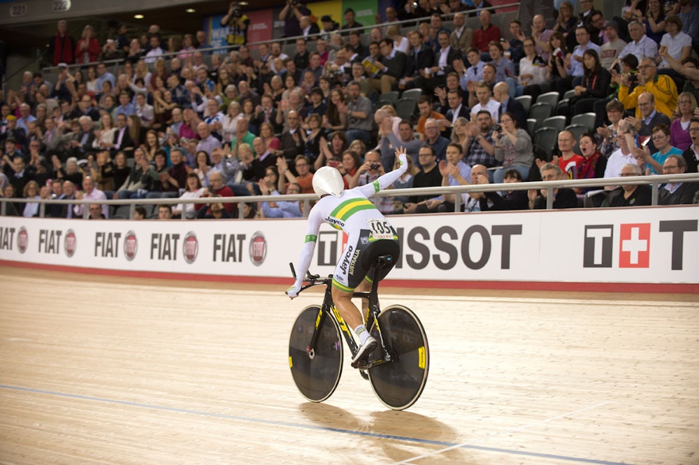 An Australian track cyclist (Rebecca Wiasak) facing away from the camera waves to the crowd after winning a track cycling race at a World Championships (Casey Gibson)