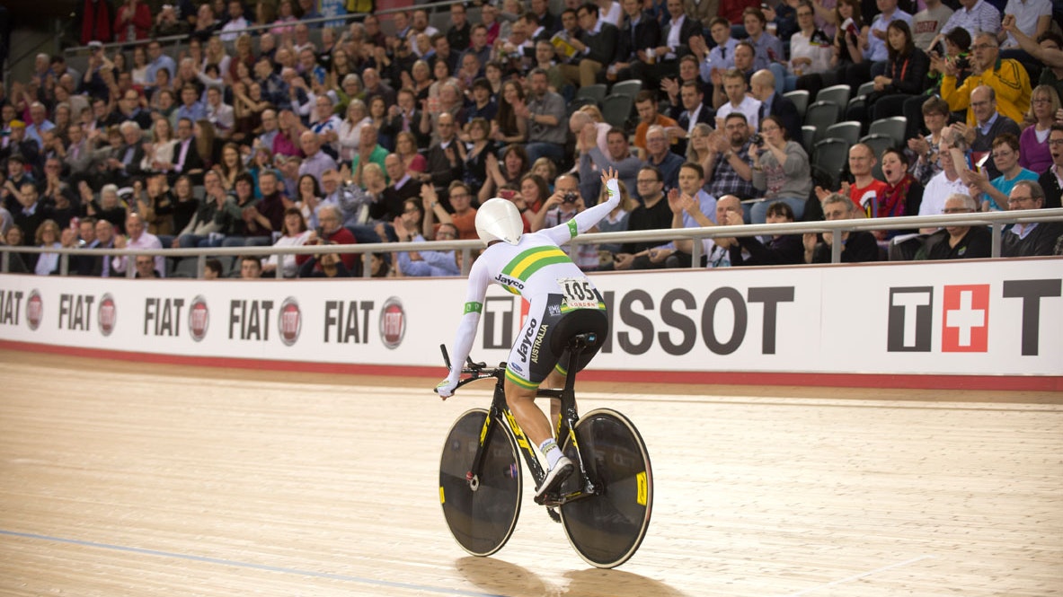 An Australian track cyclist (Rebecca Wiasak) facing away from the camera waves to the crowd after winning a track cycling race at a World Championships (Casey Gibson)