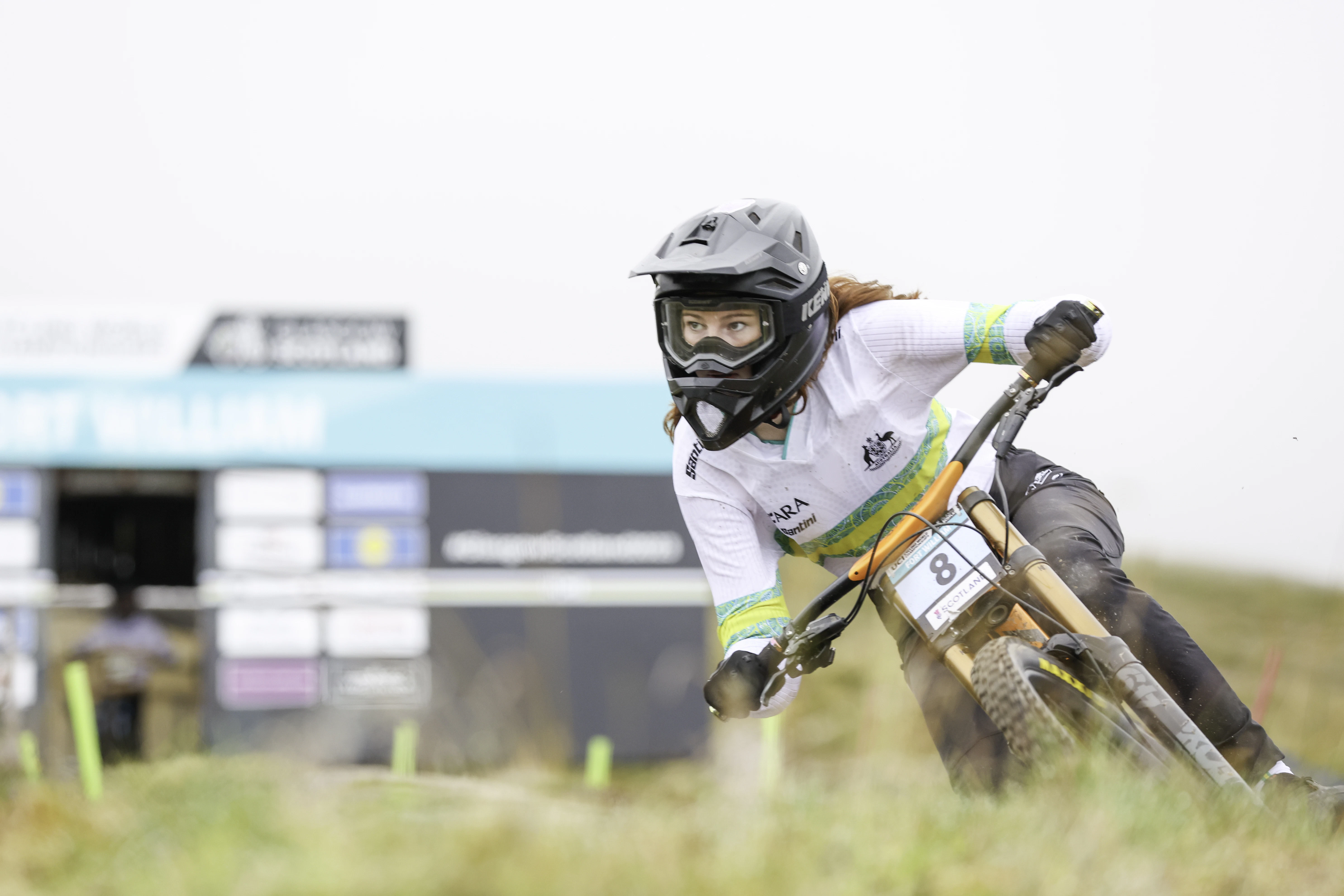 Sacha Mills leans her mountain bike into a dusty corner, wearing Australian team kit and a full face helmet.