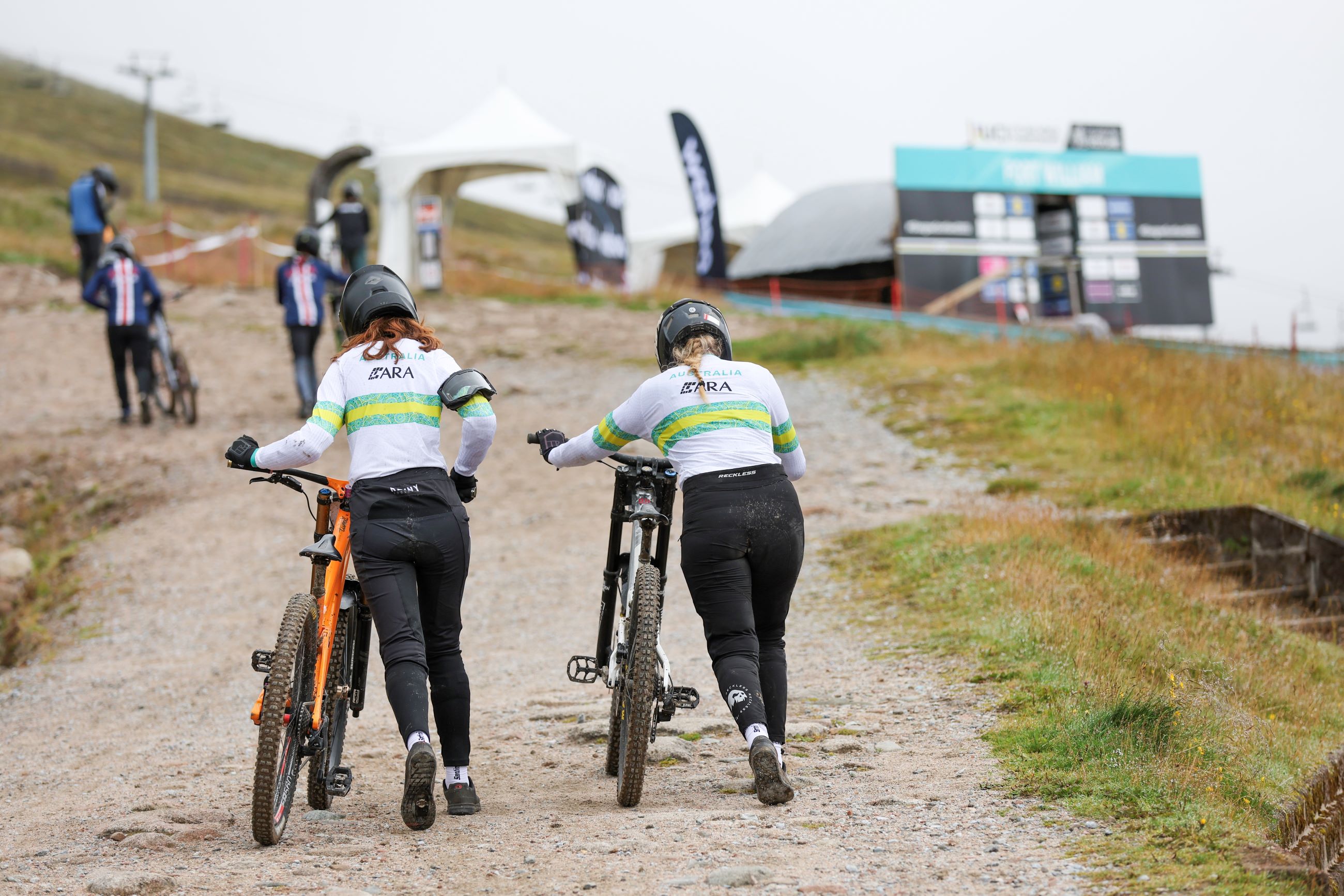 Two female ARA Australian Cycling Team downhill mountain bike athletes push their bicycles uphill towards the start at the UCI World Championships in Scotland, 2023