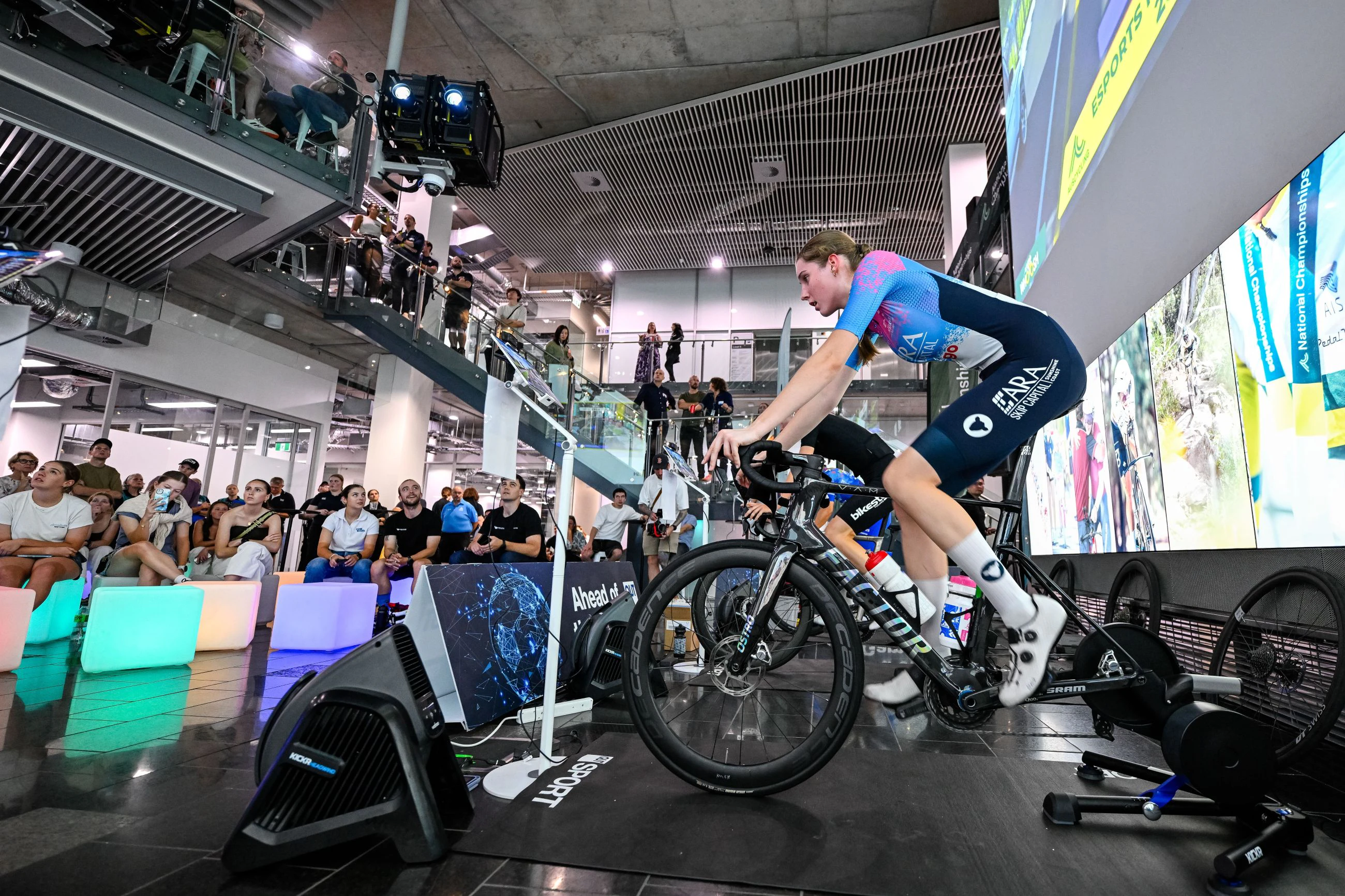 Australian cyclist Megan Moore of ARA Skip Capital competes in front of a crowd at the 2025 AusCycling Esports National Championships at The Cube, QUT Queensland University of Technology, Brisbane