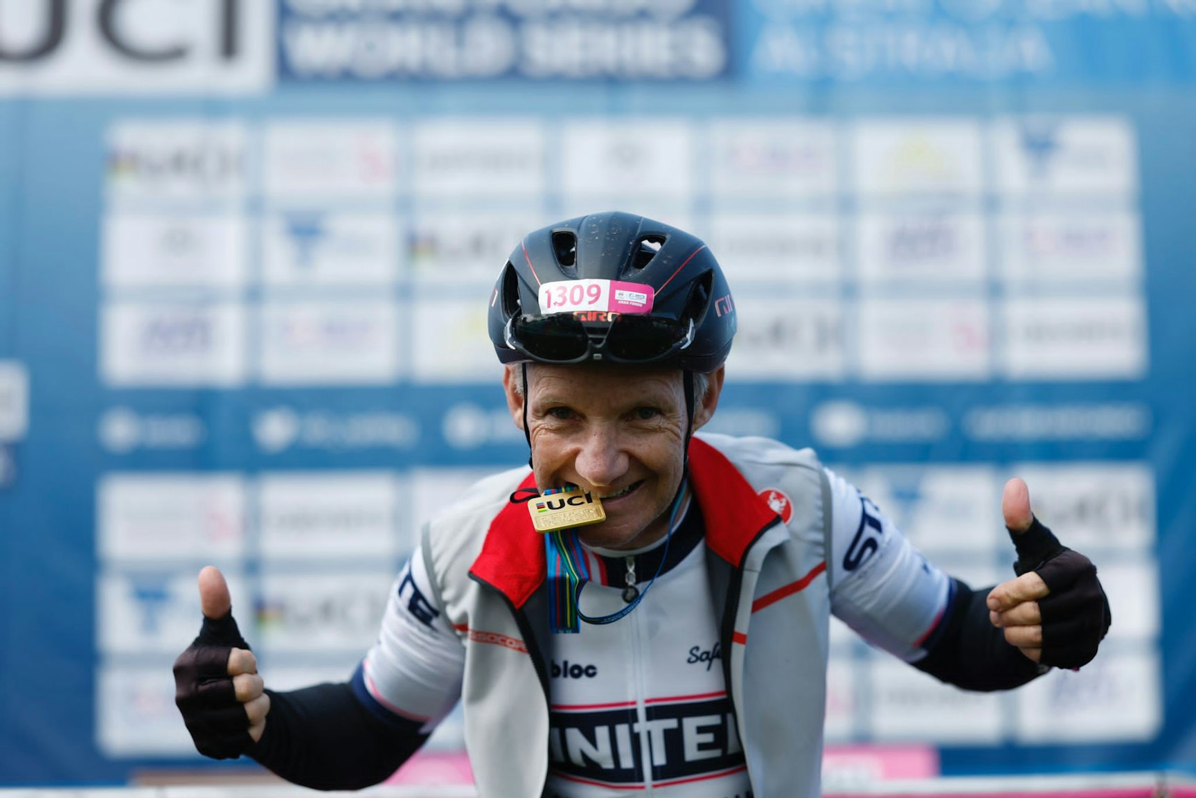 A masters-aged male road cyclist bites his UCI medal and gives two thumbs up after qualifying for the Gran Fondo World Championships at Amy's Great Ocean Road Gran Fondo.