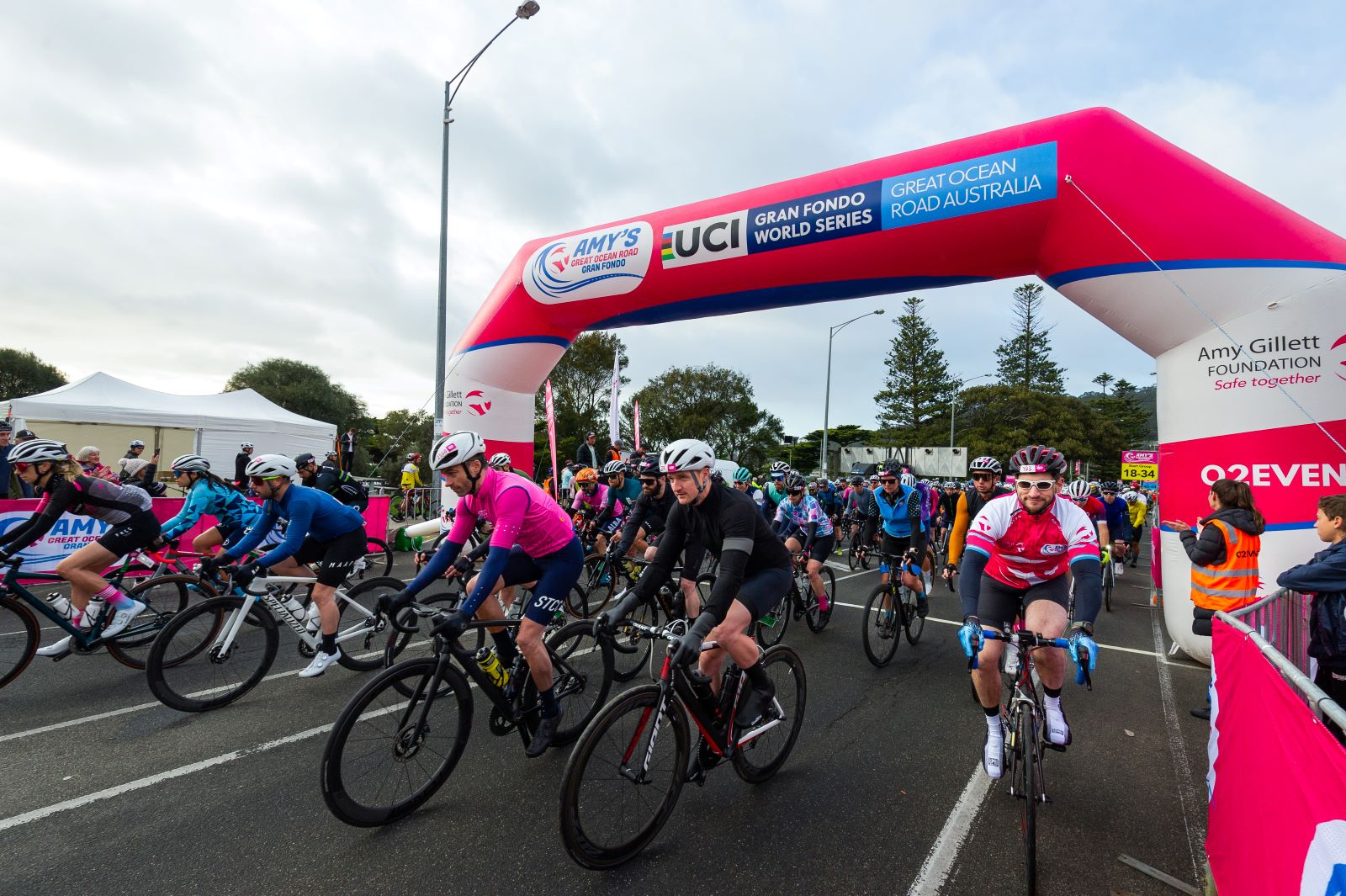 Cyclists pass under the large pink start banner at Amy's Great Ocean Road Gran Fondo.