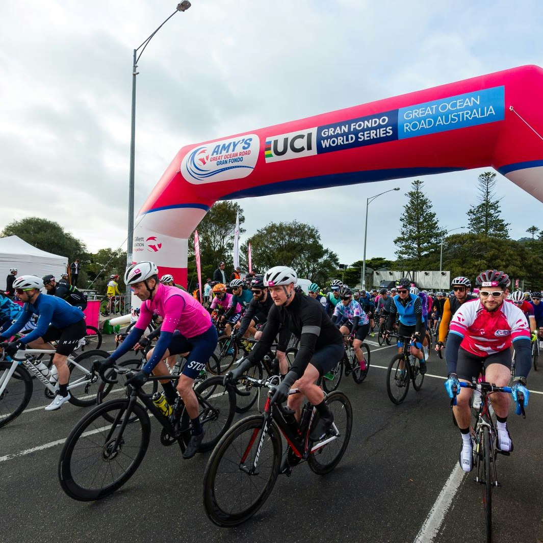 Cyclists pass under the large pink start banner at Amy's Great Ocean Road Gran Fondo.