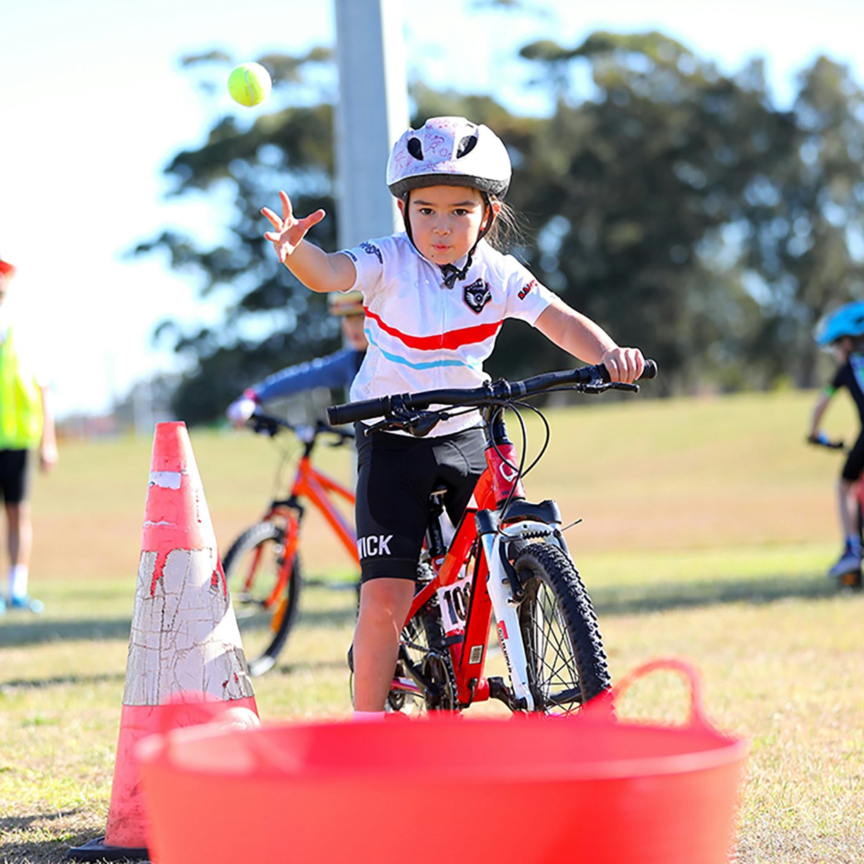 AusBike student throwing a tennis ball into a bucket while riding a bike