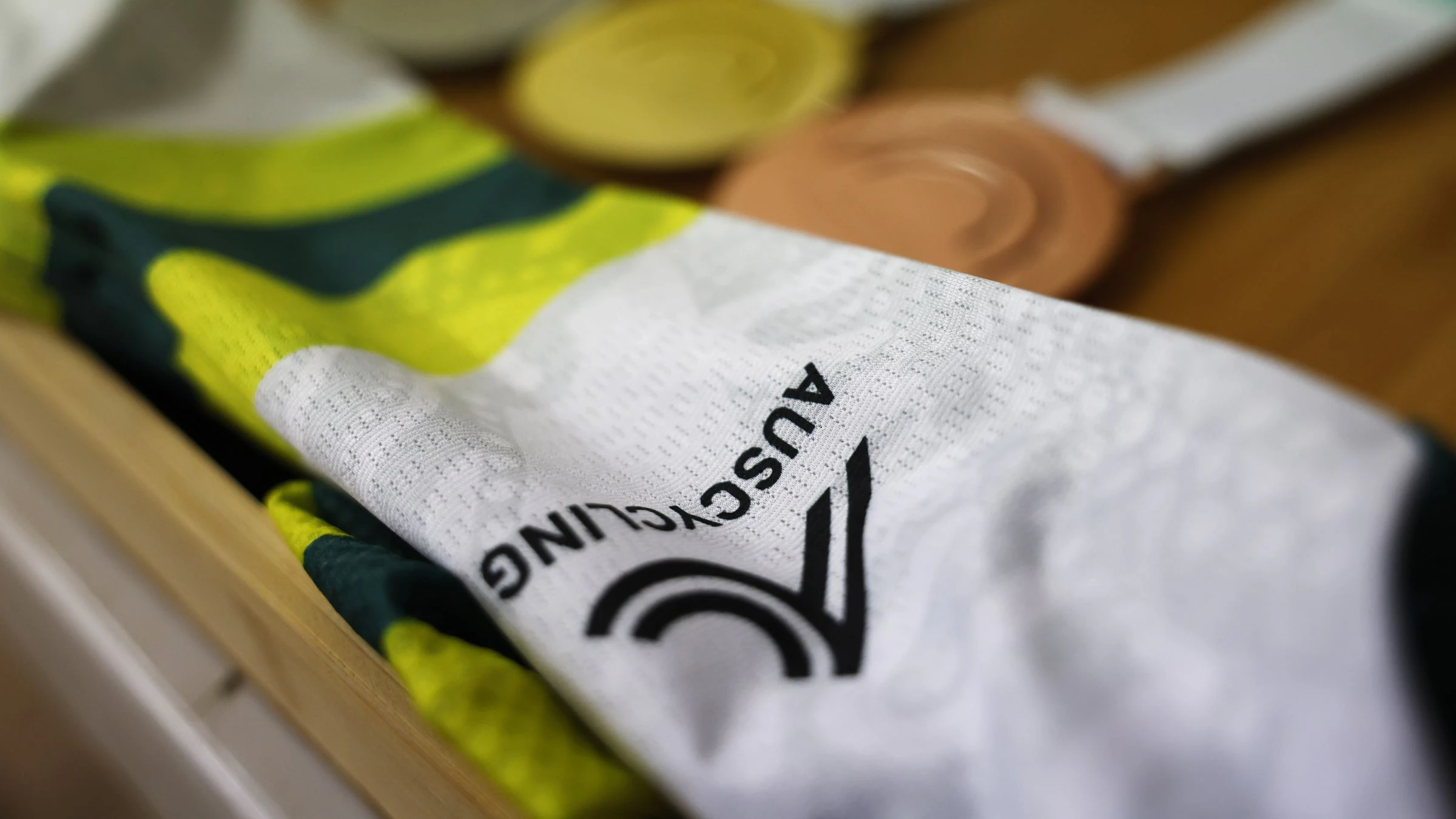 A close-up of the AusCycling logo on the green-and-gold Masters national champion jersey with a set of gold, silver and bronze medals in the background