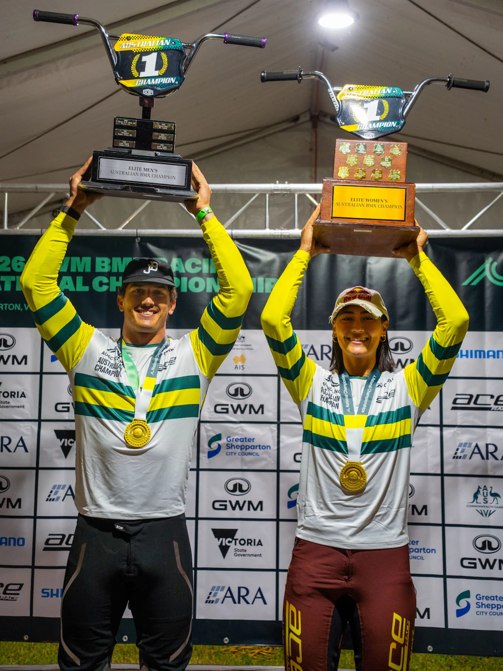 Jesse Asmus and Saya Sakakibara pose with trophies aloft, gold medal, national champion's green-and-gold jersey as elite winners at the 2026 GWM BMX Racing National Championships in Shepparton, Victoria