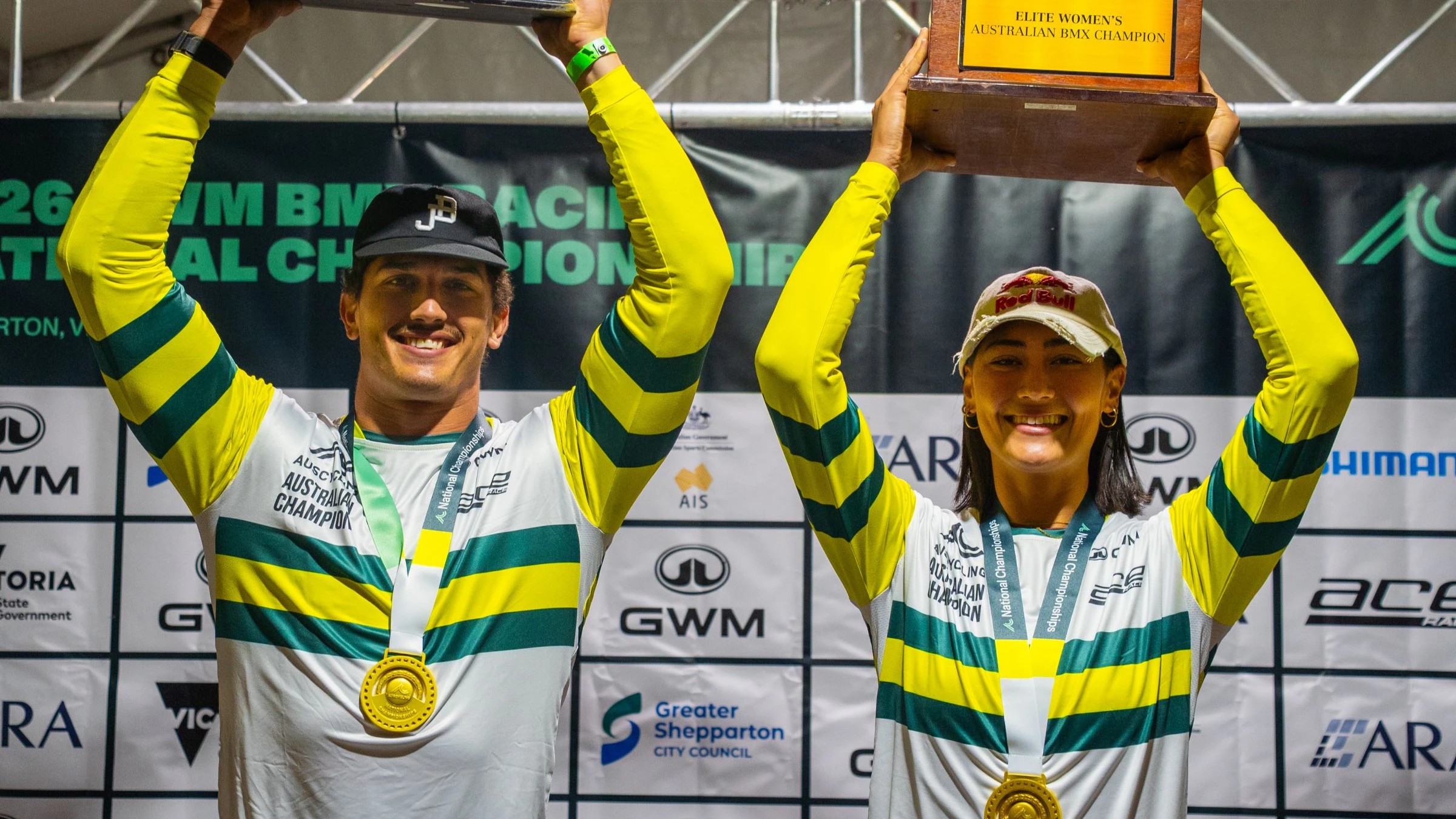 Jesse Asmus and Saya Sakakibara pose with trophies aloft, gold medal, national champion's green-and-gold jersey as elite winners at the 2026 GWM BMX Racing National Championships in Shepparton, Victoria