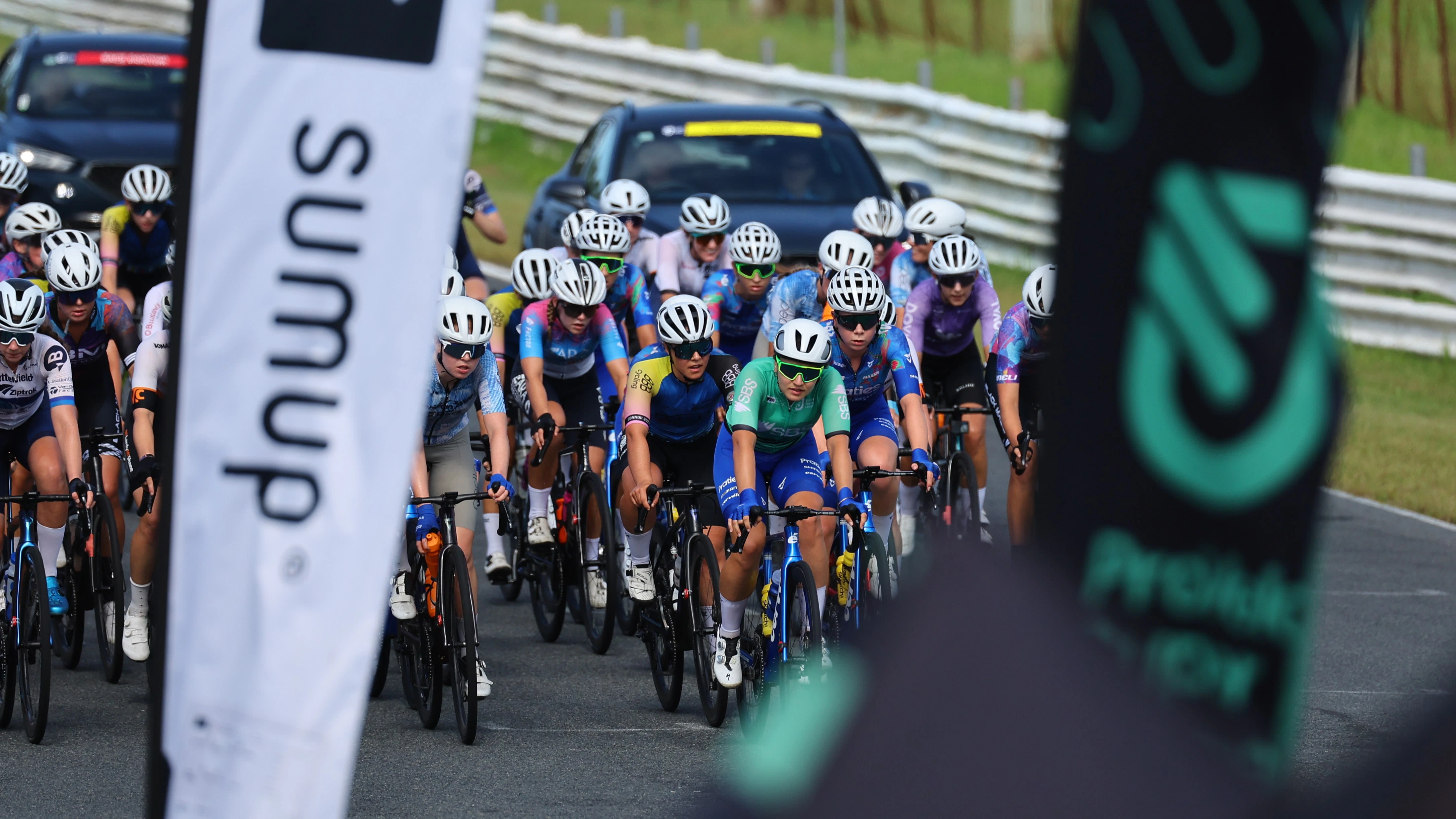 The peloton of the women's ProVelo Super League framed behind a SumUp and PSL flag