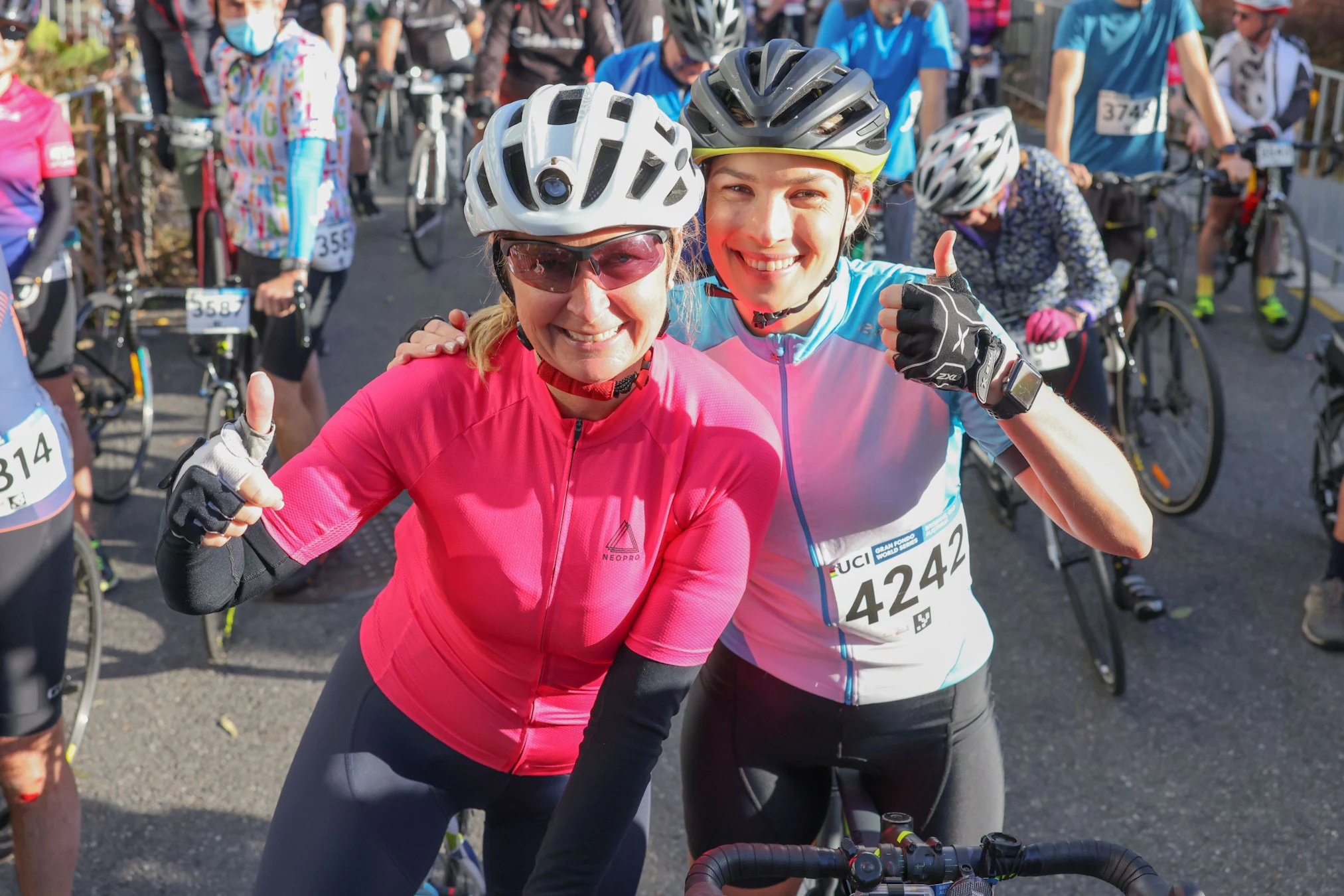 Two female recreational road cyclists smile with thumbs up at the start line of the Tour de Brisbane gran fondo participation event